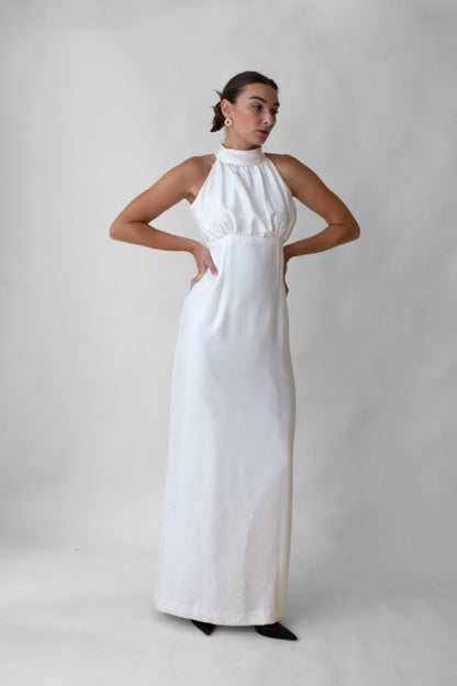 Woman wearing a white silk halter neck dress with mother of pearl button against a plain background